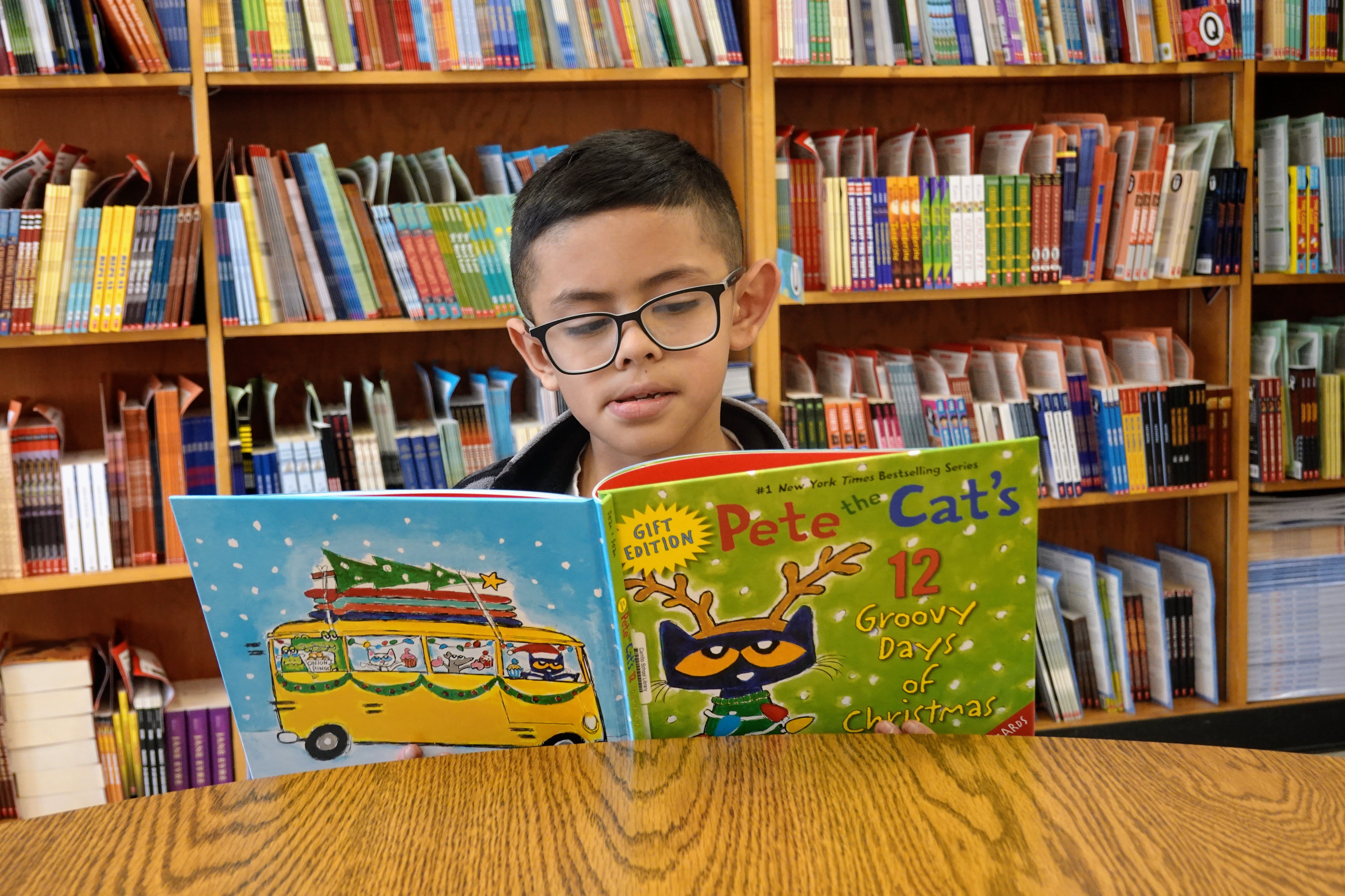 A boy with glasses reads a Pete the Cat book