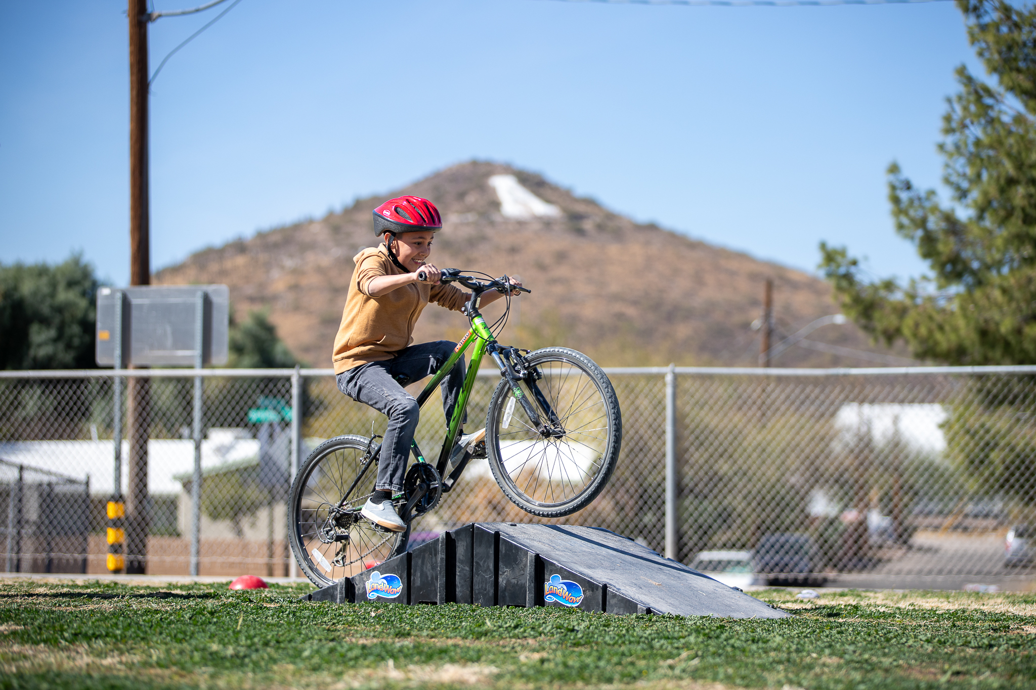 A boy rides his bike over a ramp with A Mountain in the background