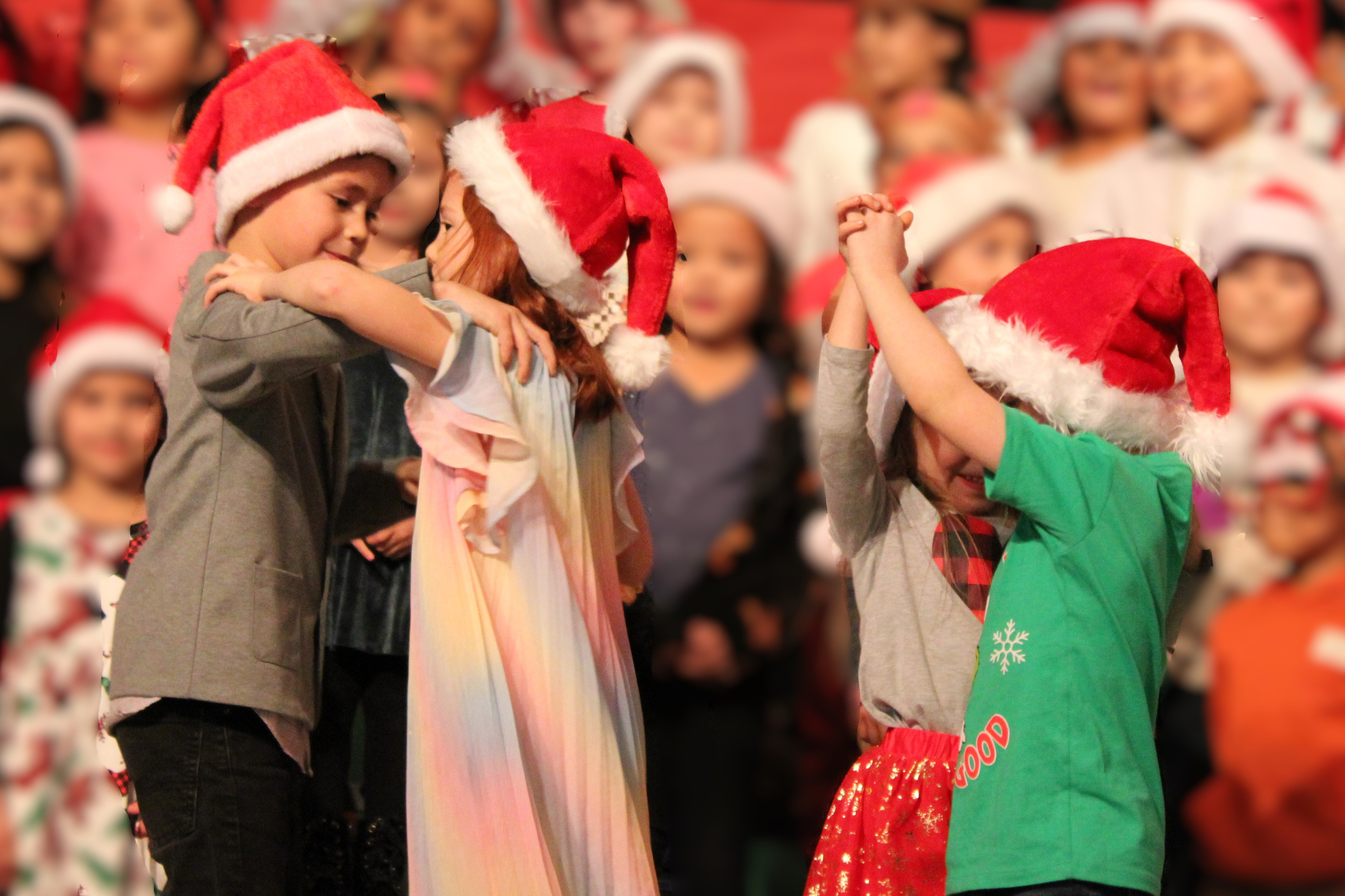 Little kids wearing Santa hats dance together