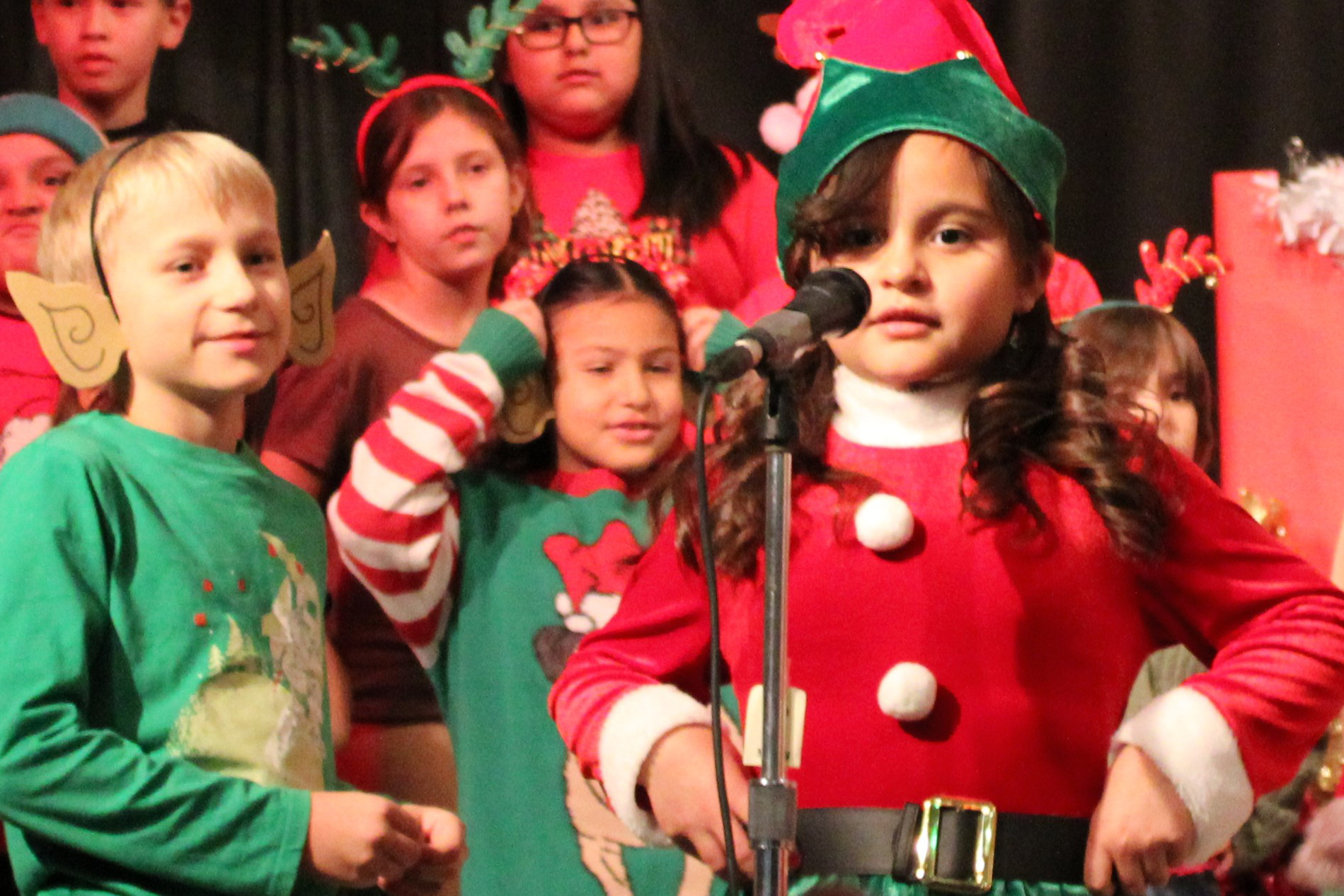 A little girl in an elf costume sings into a microphone