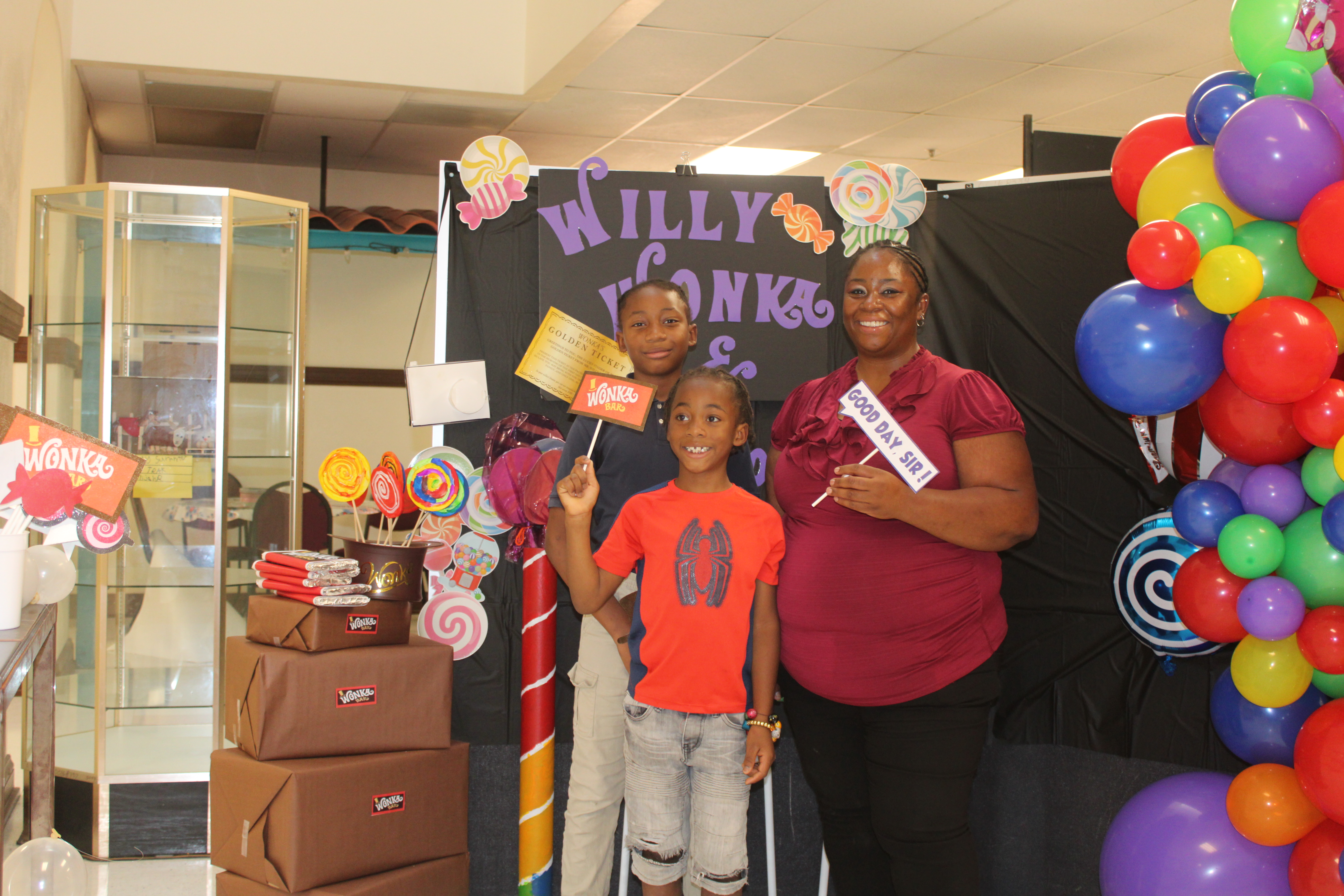 Two brothers and their mom pose with signs in front of the Willy Wonka display