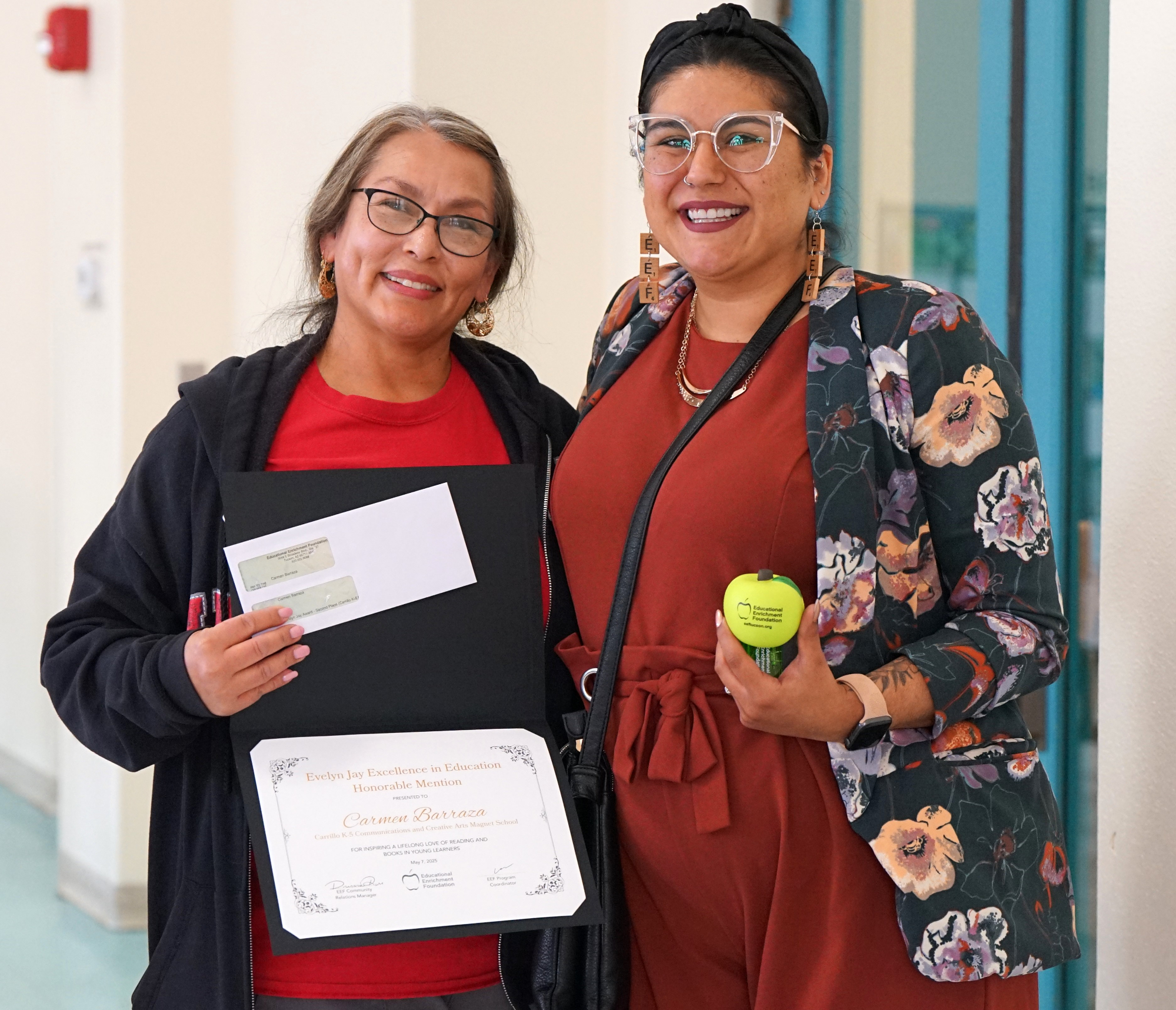 A woman proudly holds her award certificate next to a woman