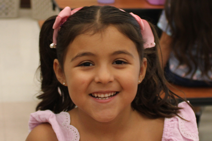 A little girl with pink hair bows smiles