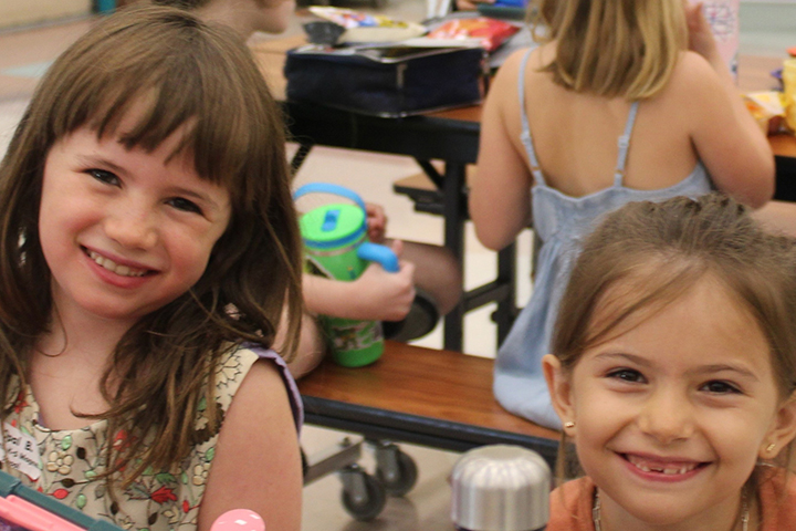 Two girls smile together at a cafeteria table