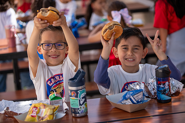 Two boys excitedly hold up their cheeseburgers