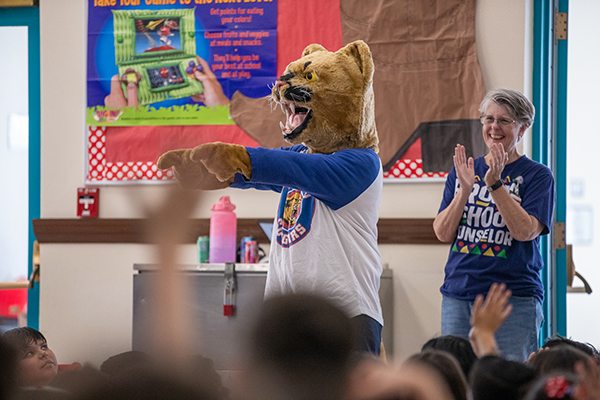 A person in a cougar mascot costume points to the crowd of students