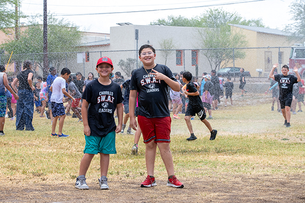 Two boys smile as their classmates get sprayed with a fire truck hose