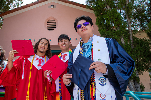 Three high school grads pose in their caps and gowns in front of Carrillo