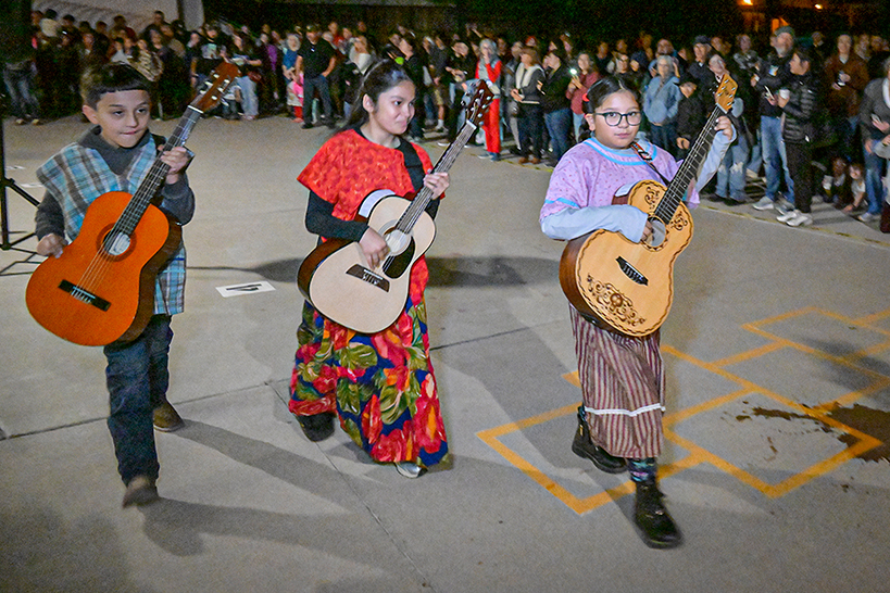Three students holding guitars walk during the procession, surrounded by families and students