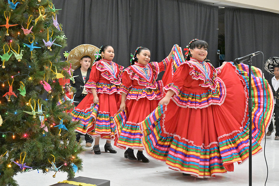 Girls wearing red folklorico dresses dance in, past a Christmas tree