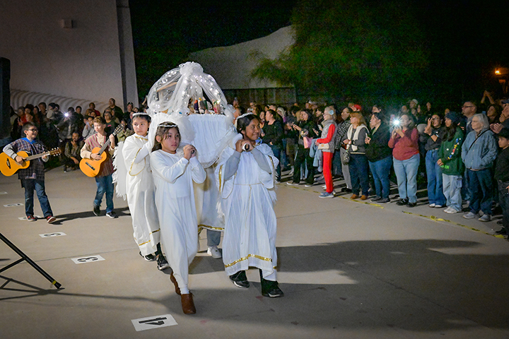 Students dressed in white robes carry in a display of the Nativity