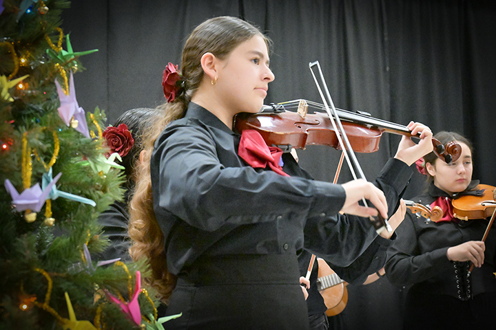 A girl plays violin in front of a Christmas tree