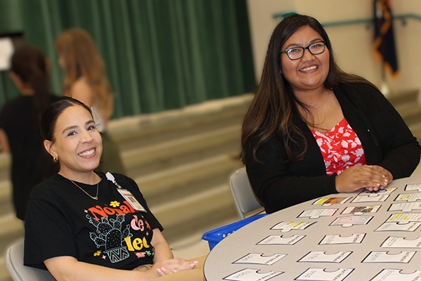 Two women smile sitting behind a table