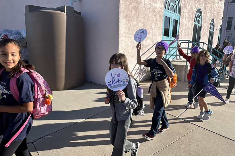 Students walk around campus holding signs that say Go Ruby!