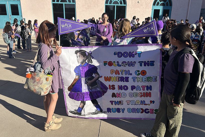 Students hold up a banner that says Don't follow the path, go where there is no path and begin the trail