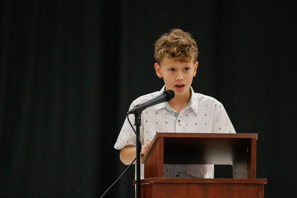 A boy stands behind a podium and talks into a microphone