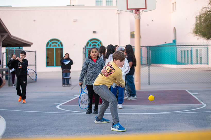 A boy in a yellow shirt swings at a tennis ball