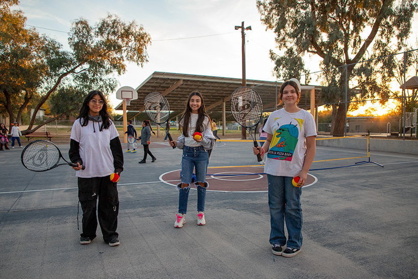 Three girls smile holding their tennis racquets