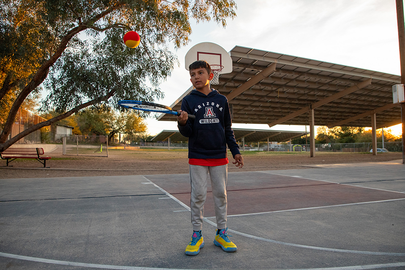 A boy in a UofA sweatshirt bounces a tennis ball off a racquet