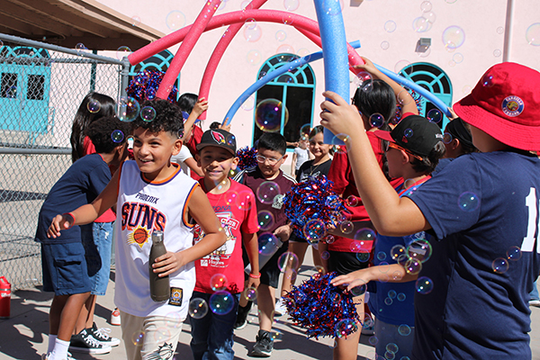 Students hold up pool noodles as an arch for classmates to run under