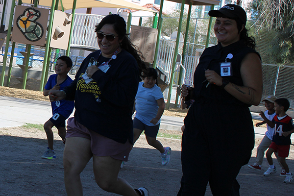 Two women run around the playground next to their students
