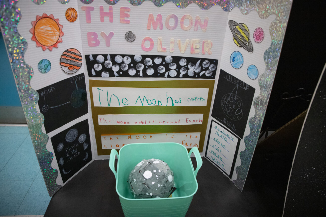 A cardboard setup with the words The Moon by Oliver and cutouts of the sun and planets