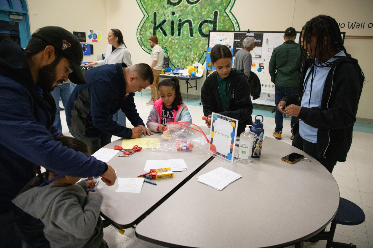 Parents and students stand around a table working on space-themed crafts
