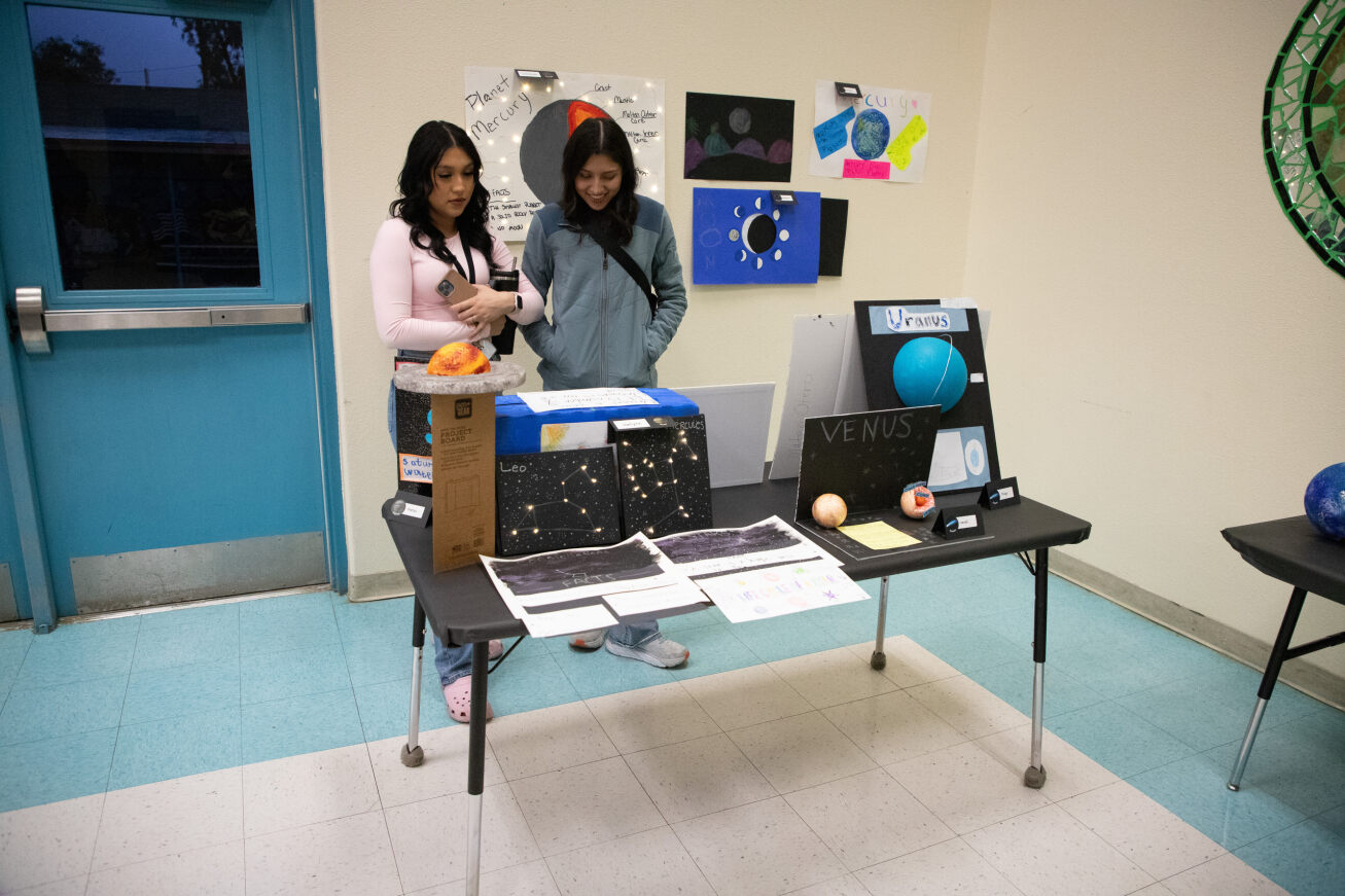 Two women look at a table filled with space-themed science projects