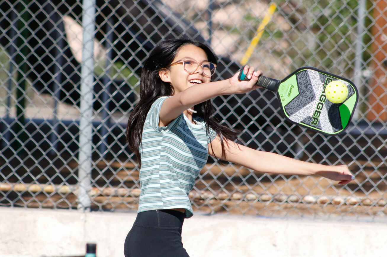 A girl in glasses smiles as she hits the ball over the net