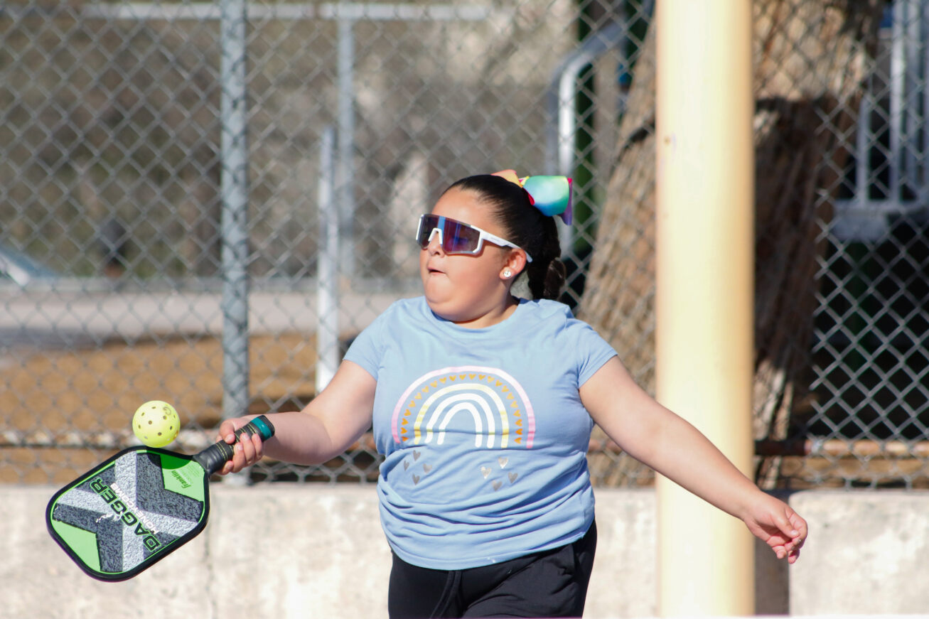 A girl in sunglasses aims her racquet at the ball