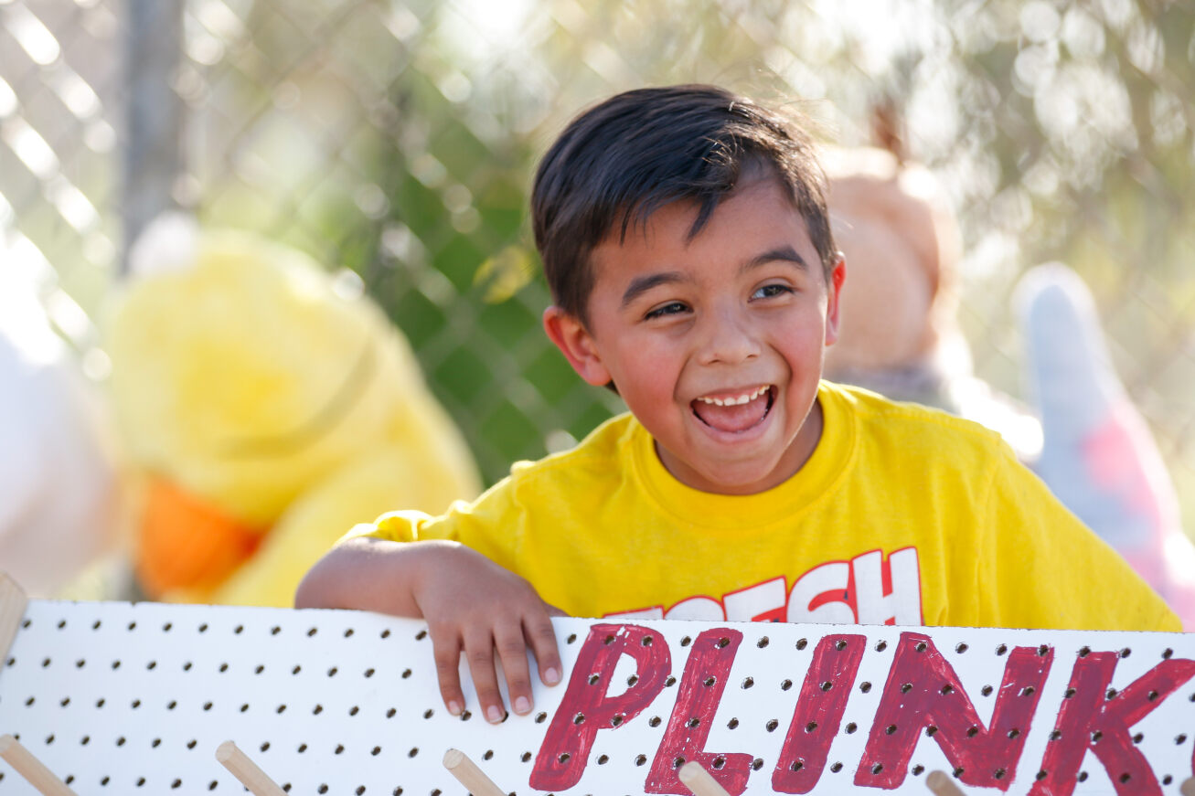 A little boy in a yellow shirt smiles while playing plinko